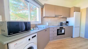 A compact kitchen with a microwave, washing machine, oven, and a refrigerator. - The Urban Oasis: Comfort 2br near the City Center! (Larnaca)