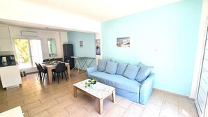 Ein modernes Wohnzimmer mit einem hellblauen Sofa, einem Couchtisch aus Holz mit einer Pflanze und einem Essbereich mit Tisch und Stühlen.