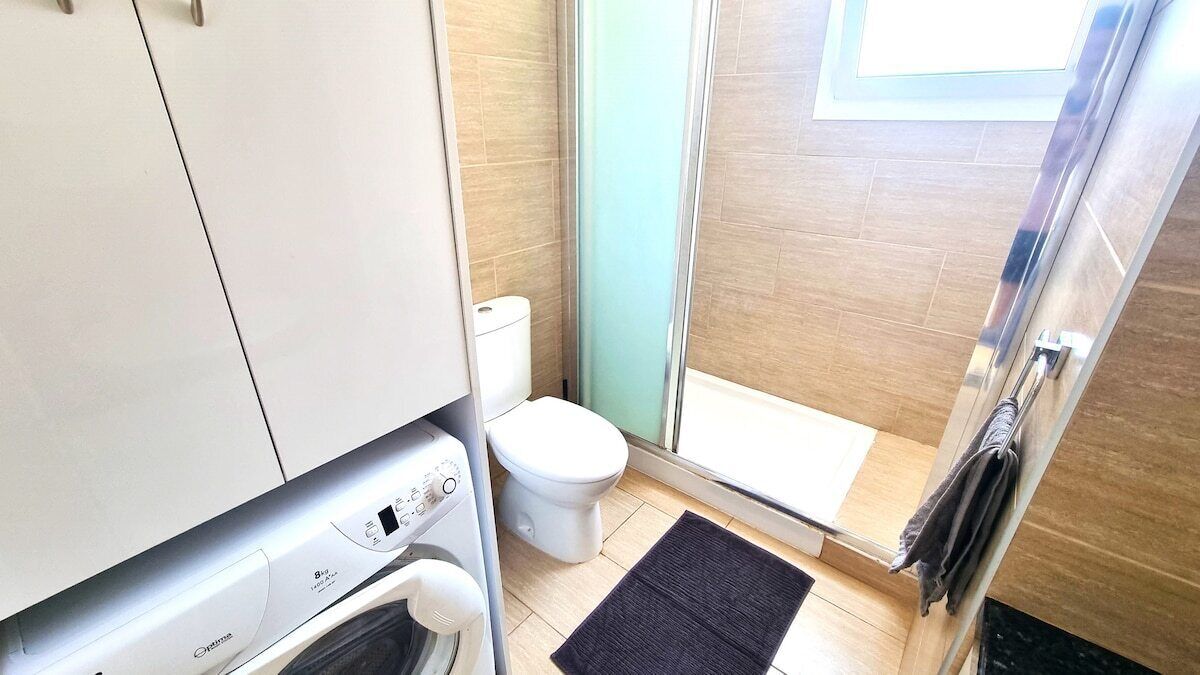 Un baño pequeño con lavadora, inodoro y cabina de ducha de vidrio.