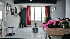 A modern living room with a sofa, a coffee table, and a dining table. - Cozy Sea View Apt w/ pool access + Netflix (Larnaka)