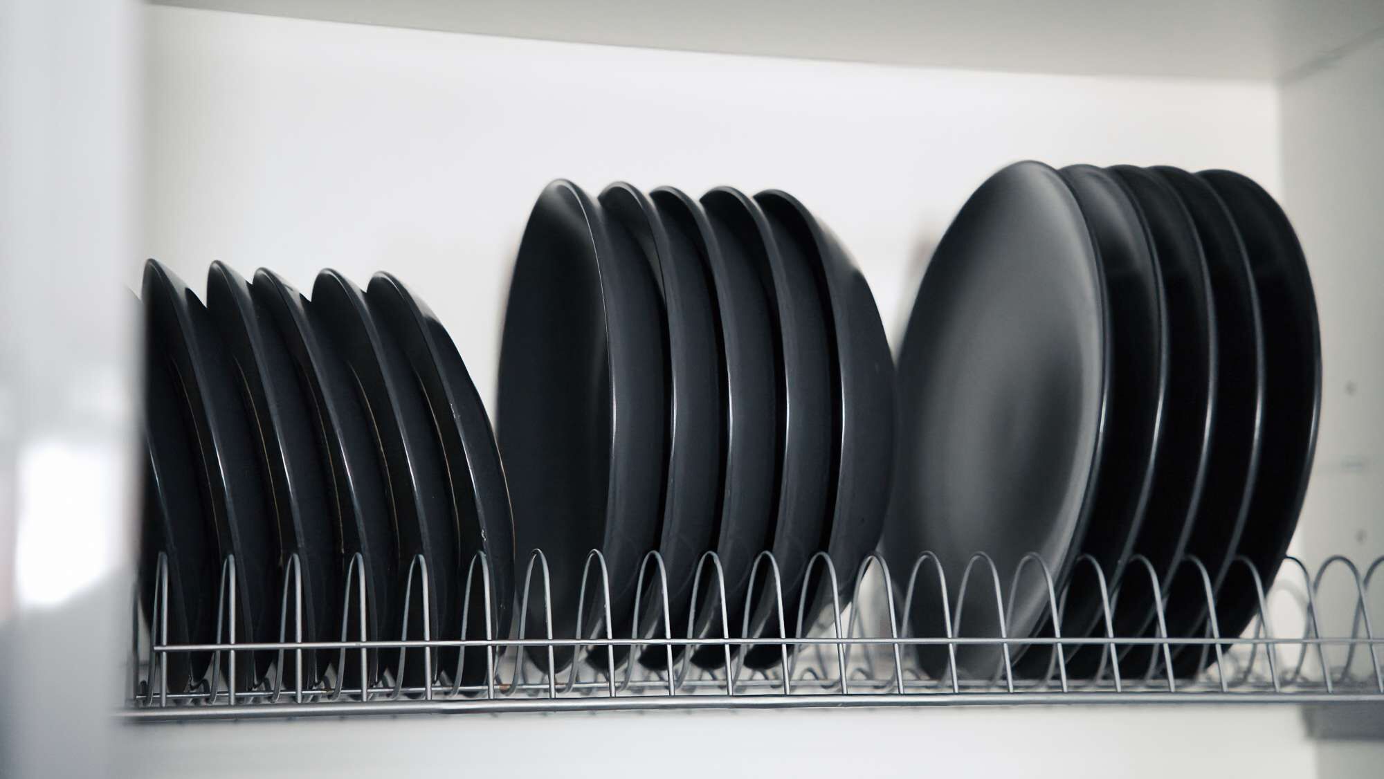 Un escurreplatos metálico con platos y cuencos negros organizados en una cocina.