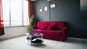 Un salon moderne avec un canapé rouge, une table basse en verre, une plante en pot et une vue par la fenêtre.