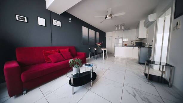 A modern living room with a red sofa, a coffee table with a plant, and a dining area with a white table and chairs. - Cozy Sea View Apt w/ pool access + Netflix (Larnaka)