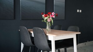 Une table à manger avec des chaises, un vase rempli de fleurs et un mur noir orné d’un tableau.