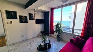 Un salon moderne avec une table basse en verre, un canapé rouge et une grande fenêtre donnant sur la mer.