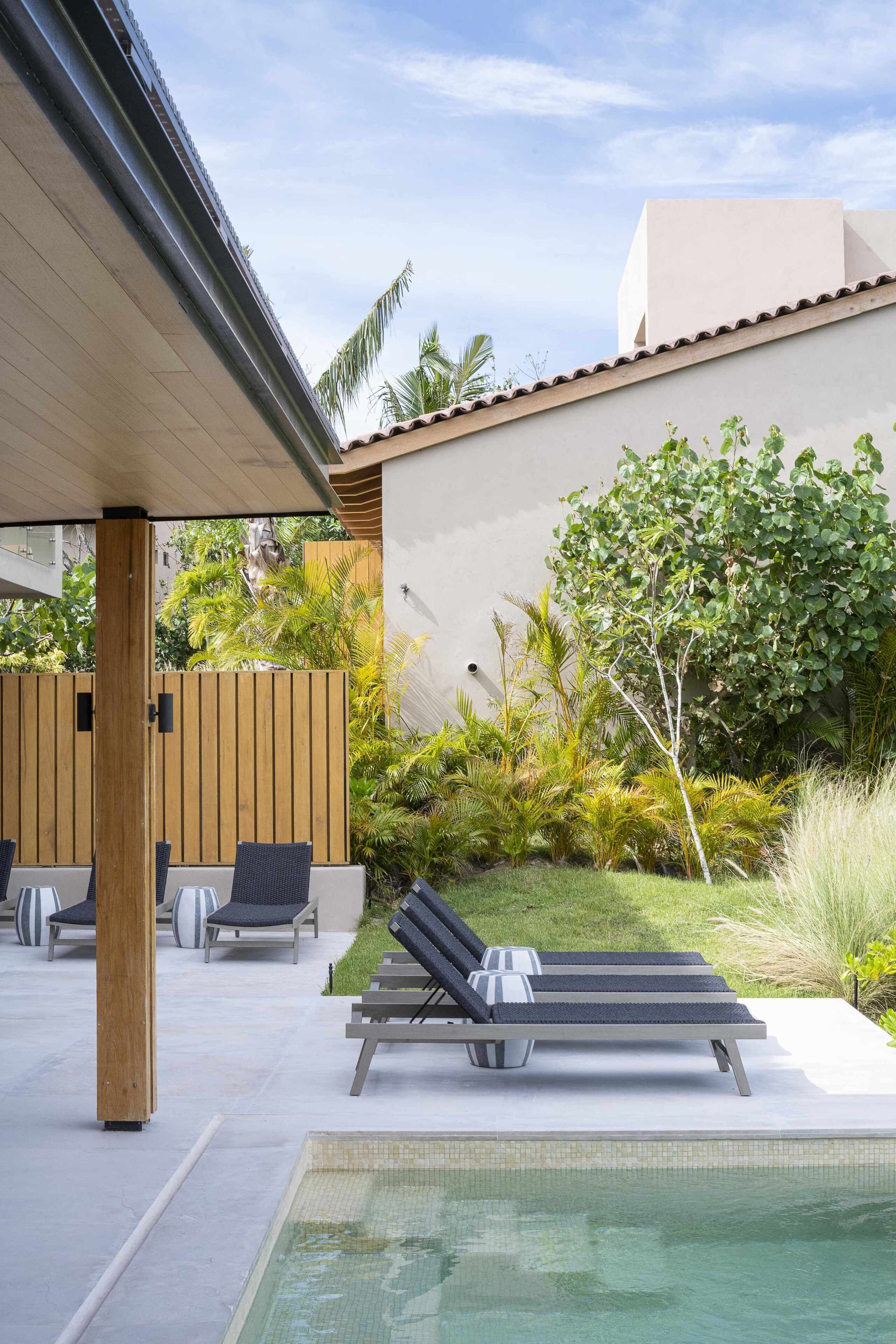 A modern outdoor pool area with lounge chairs and a wooden fence.