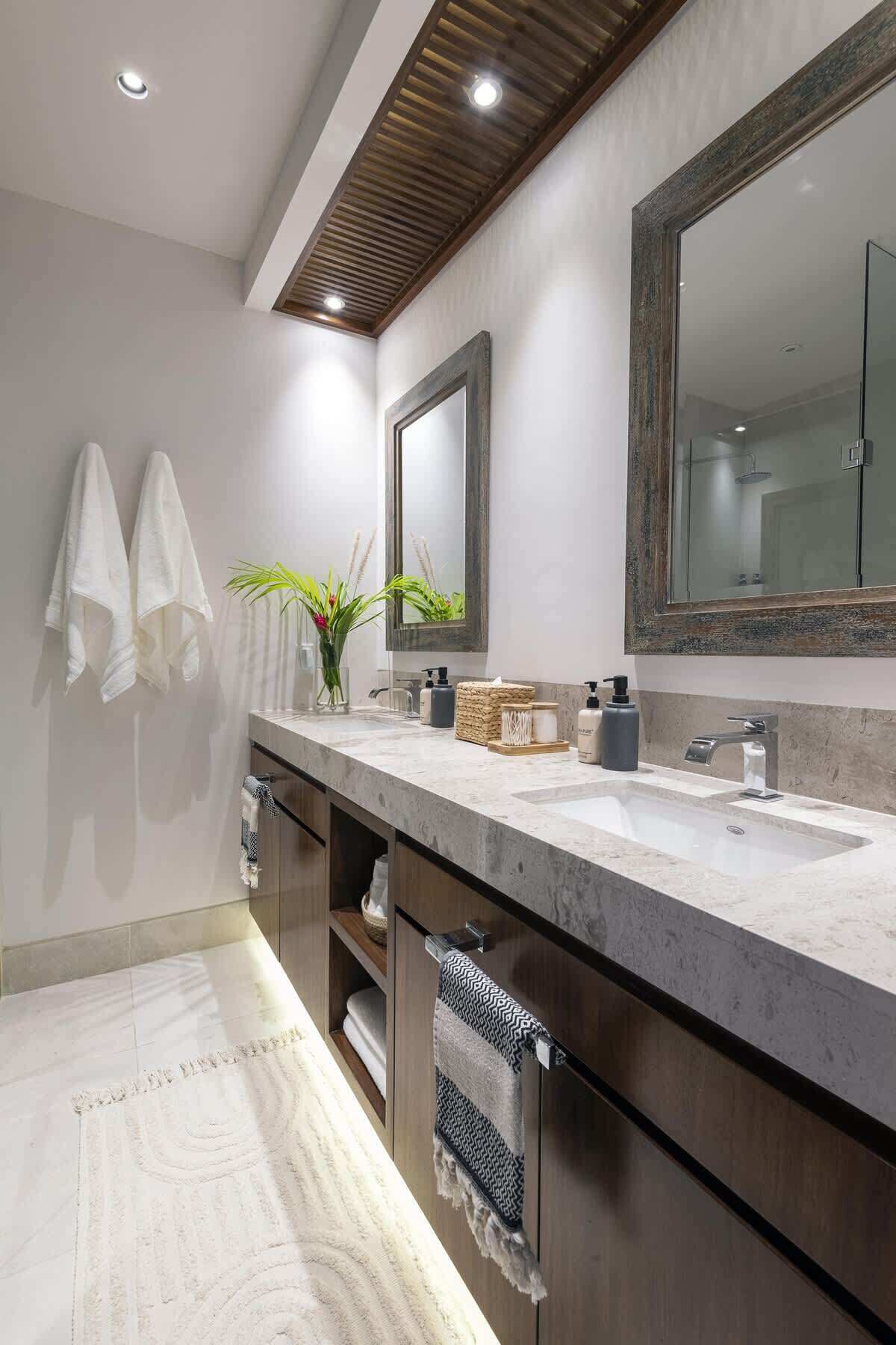 Une salle de bain moderne avec un grand miroir, un meuble-lavabo doté d’un plan en marbre et deux serviettes accrochées au mur.