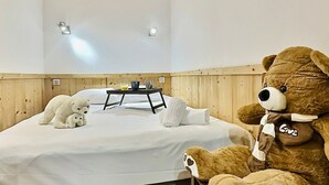 A bedroom with a bed, a wooden headboard, a bedside table with a lamp, and a large teddy bear.