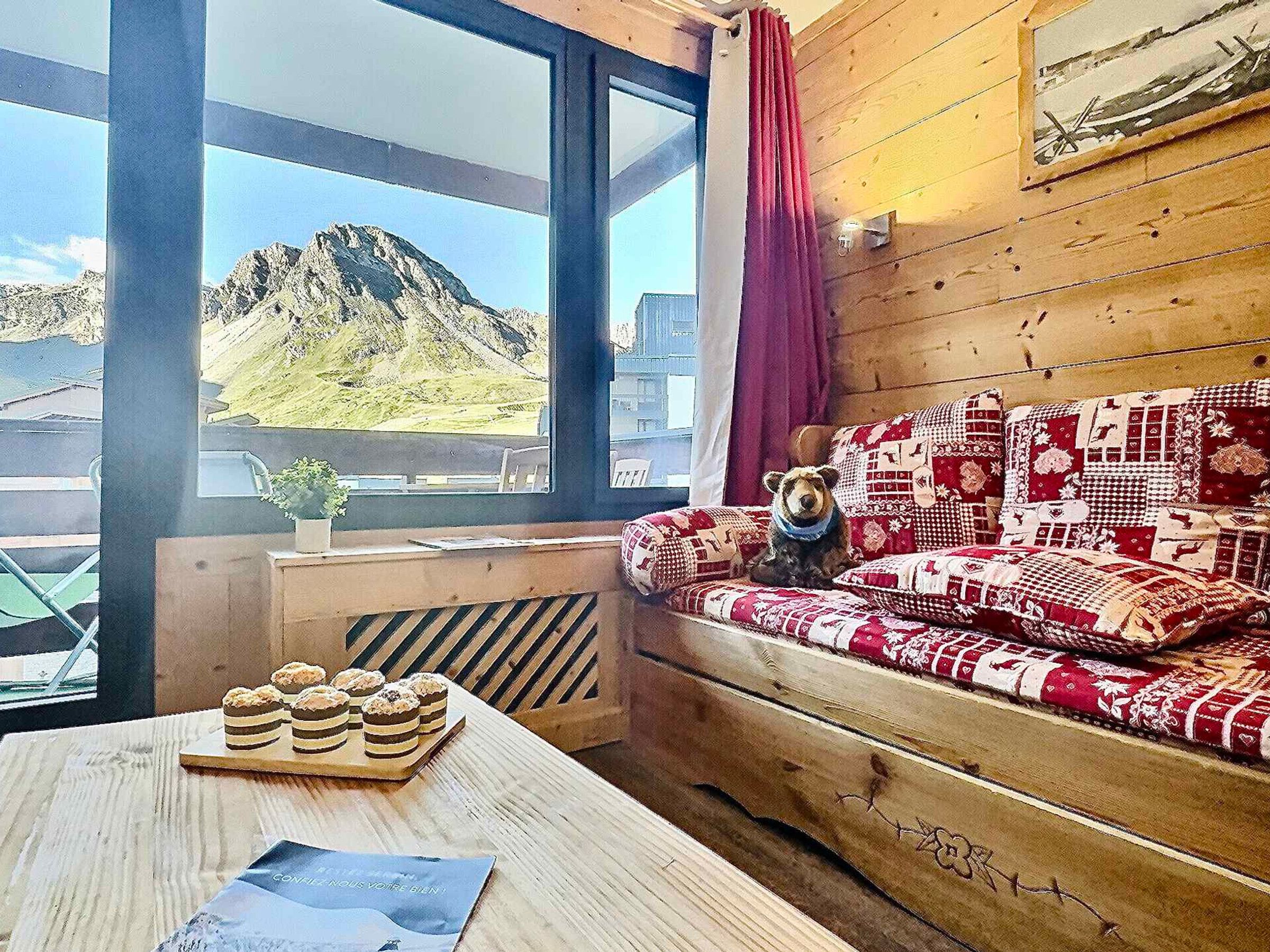 A cozy room with a wooden sofa, a teddy bear, and a table with pastries.