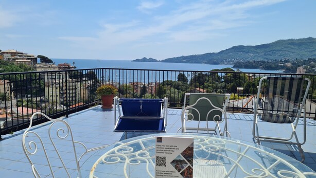 A balcony with a table, chairs, and a sign about booking a boat tour. - Grande Attico by PortofinoVacanze (Rapallo)