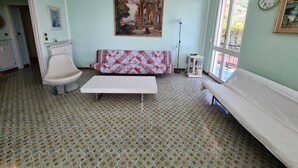 A room with patterned floor tiles, a white sofa, a white chair, a painting on the wall, and a window with a view. - Grande Attico by PortofinoVacanze (Rapallo)