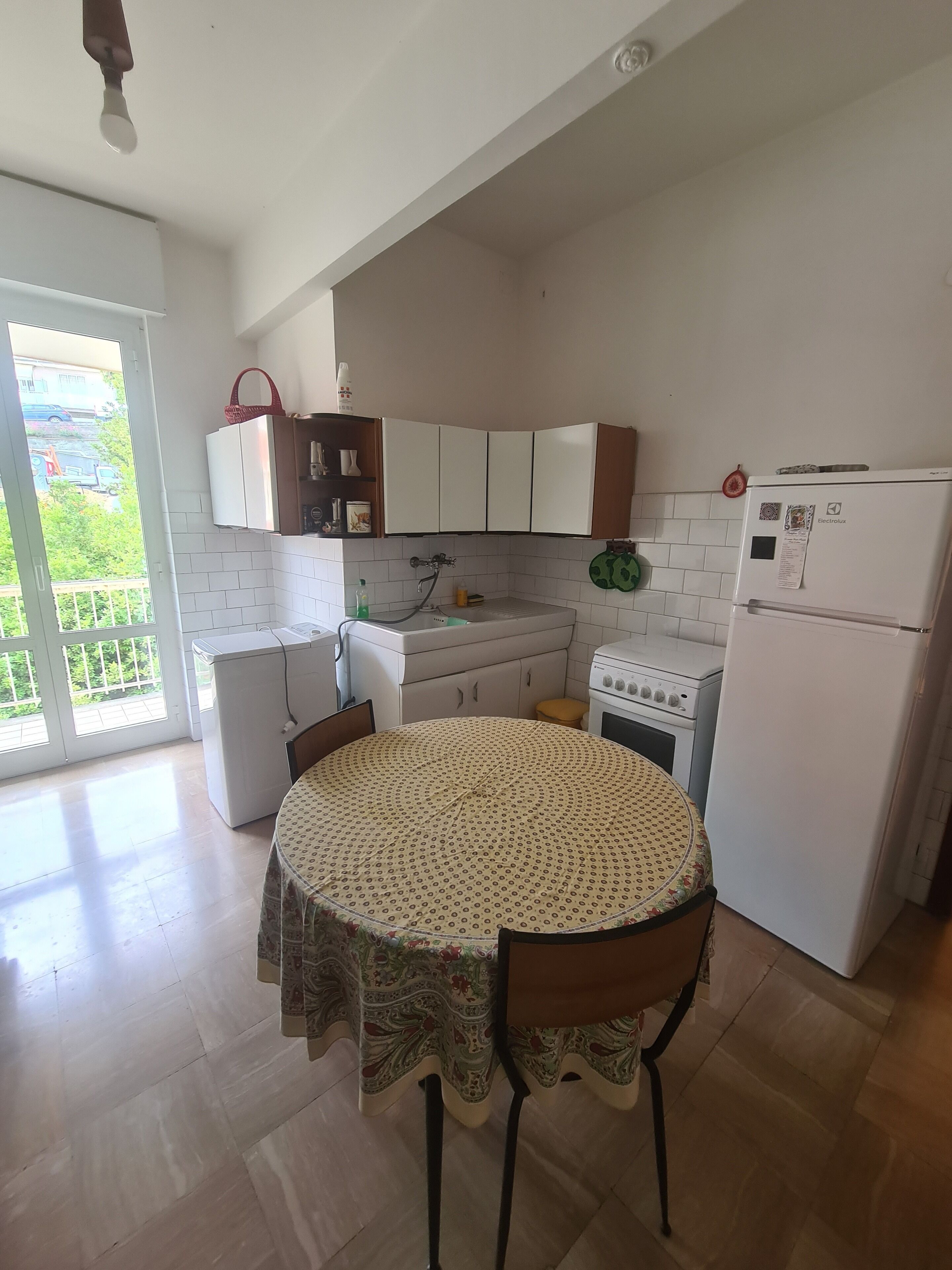 A kitchen with white cabinets, a stove, a refrigerator, and a dining table with a patterned tablecloth.