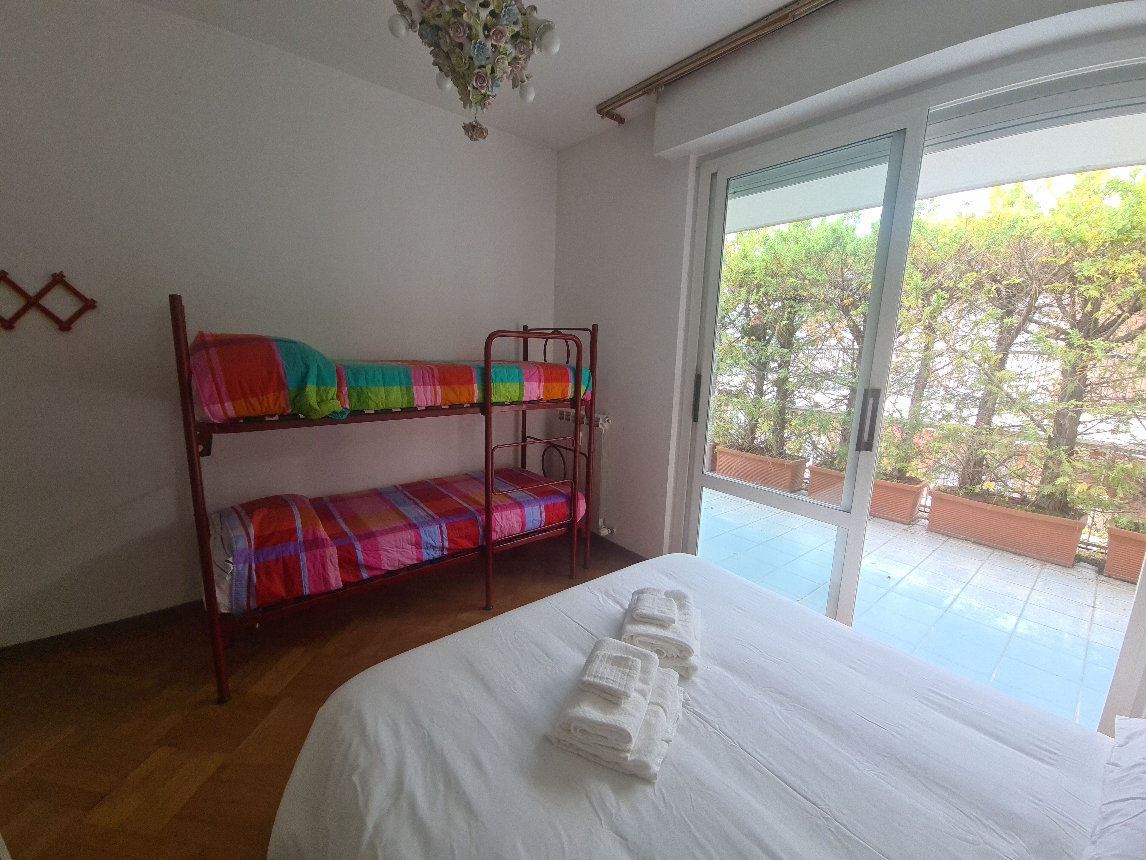A room with bunk beds, a large bed with white linens, and a view of trees through a glass door.