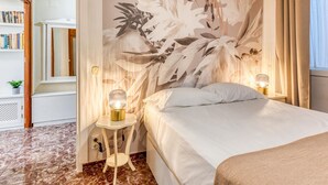 Ein Hotelzimmer mit einem Bett, einem Nachttisch mit Lampe, einem Bücherregal und einem großen Wandbild.