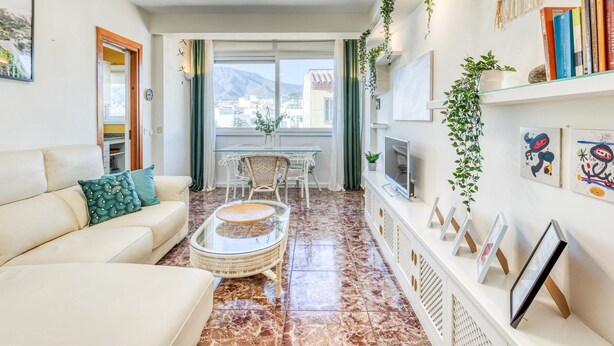 Ein modernes Wohnzimmer mit einer Couch, einem Glastisch, einem Fernseher und einem Balkon mit Blick auf Stadt und Berge.
