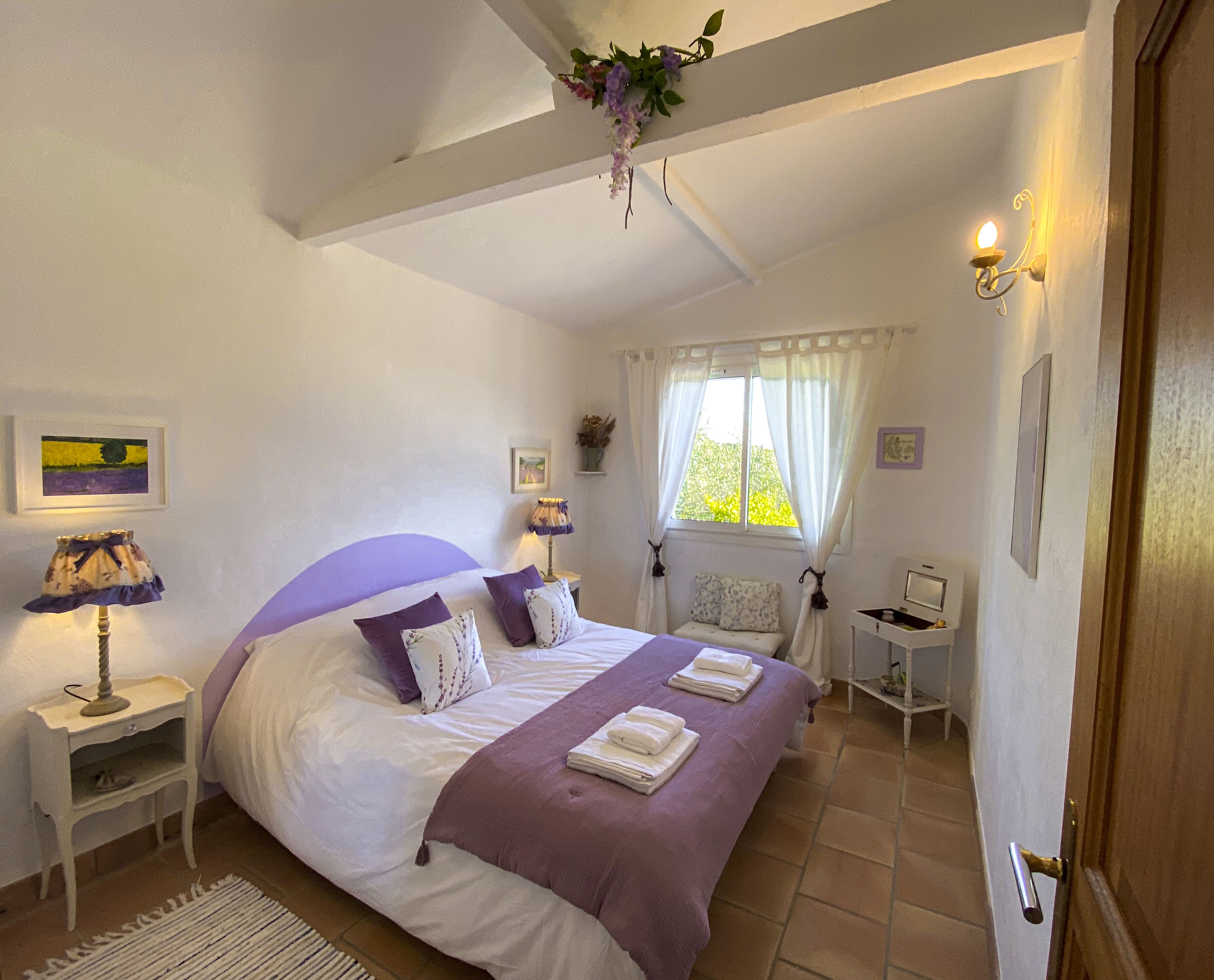 A bedroom with a large bed, two bedside tables, a nightstand, a window with curtains, and a door.
