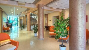 A spacious lobby with a central staircase, orange seating, and potted plants. - PRESTIGE CITY2  (Primorsko)