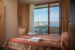 A hotel room with a bed, a desk, a chair, and a balcony with a view.