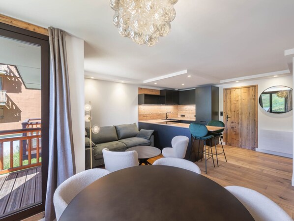 Un salon moderne comprenant un canapé, des fauteuils, une table à manger, un coin cuisine et un balcon.