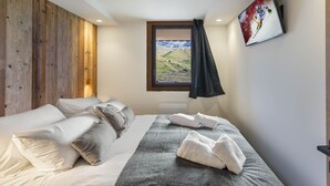A bedroom with a bed, pillows, a blanket, towels, a window with a view, and a painting on the wall. - Renovated 2-bedroom apartment in Val Thorens with WiFi (Val Thorens)