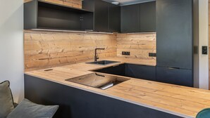 A modern kitchen with a wooden backsplash, dark cabinetry, and a built-in sink. - Renovated 2-bedroom apartment in Val Thorens with WiFi (Val Thorens)