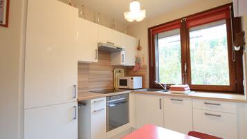 Une cuisine moderne avec des meubles blancs, un four à micro-ondes, une cuisinière et une fenêtre agrémentée de rideaux rouges.