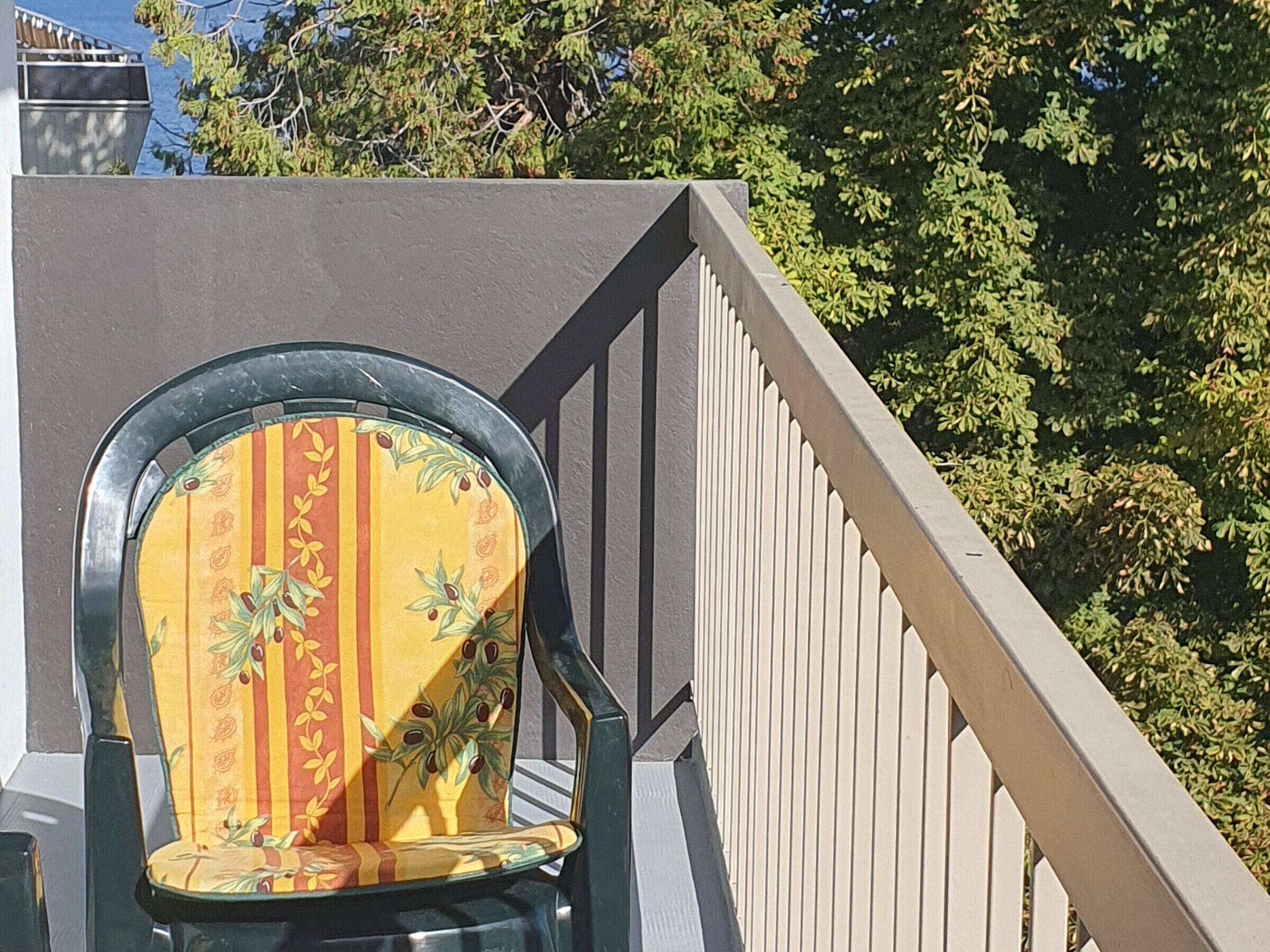 Een stoel met een gestreept kussen en metalen frame, geplaatst tegen een grijze muur met een witte leuning.