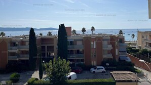 A residential building with balconies, a parking area, and a view of the sea.