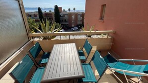 A balcony with a table and chairs, overlooking a coastal area with buildings and palm trees.