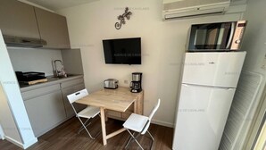 A compact kitchen with a wooden table, two white chairs, a toaster, a coffee maker, a TV, a microwave, and a refrigerator. - Studio cabin 100m from beach and shops with air conditioning and parking (Cavalaire-sur-Mer)