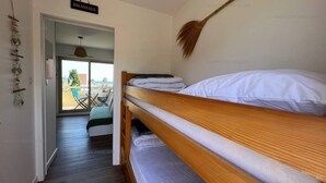 A bunk bed room with a broom on the wall, a sign reading "BIENVENUE", and a view of the outside balcony.