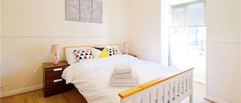 A bedroom with a bed, bedside tables, a lamp, a window, and a wall art piece.