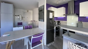 A compact kitchen with a refrigerator, stove, and a dining area with a table and chairs. - Modern T3 in Central Cavalaire - Walk to Beach & Shops, Parking, A/C, Spacious Terrace (Cavalaire-sur-Mer)