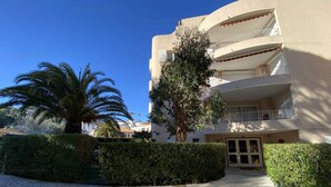 A modern building with a curved facade, multiple balconies, and a paved entrance area with surrounding greenery. - Modern T3 in Central Cavalaire - Walk to Beach & Shops, Parking, A/C, Spacious Terrace (Cavalaire-sur-Mer)