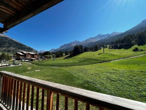 A mountain lodge with a wooden deck overlooking a green valley and mountains.