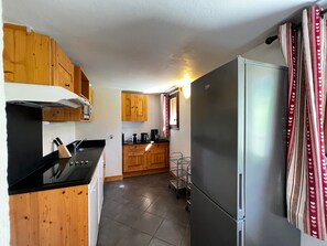 A compact kitchen with wooden cabinets, a stainless steel refrigerator, and a black countertop.