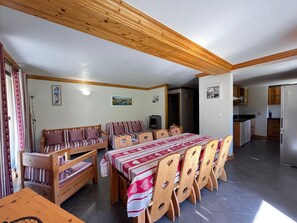 A dining area with a wooden table and benches, a kitchen with wooden cabinets, and a hallway leading to another room.
