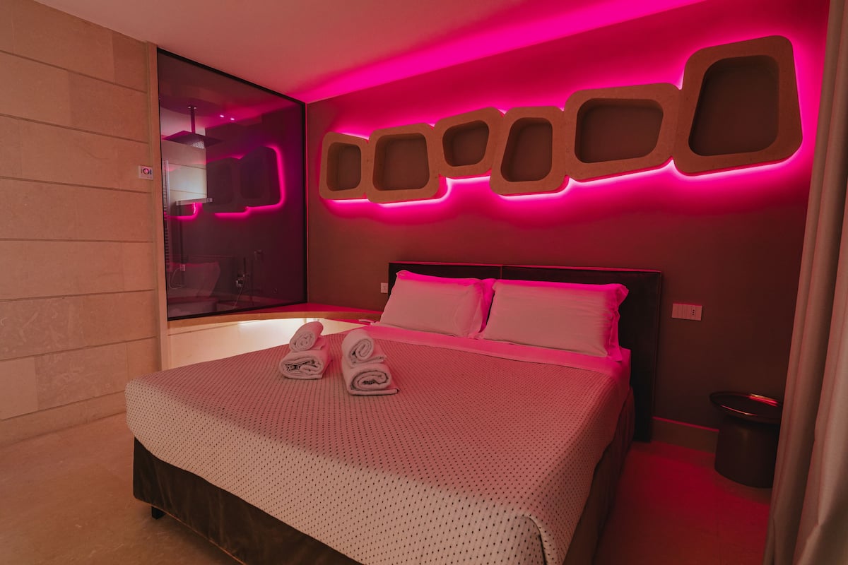 Ein modernes Hotelzimmer mit einem großen Bett, rosigem Ambiente und einem außergewöhnlichen Wanddesign.
