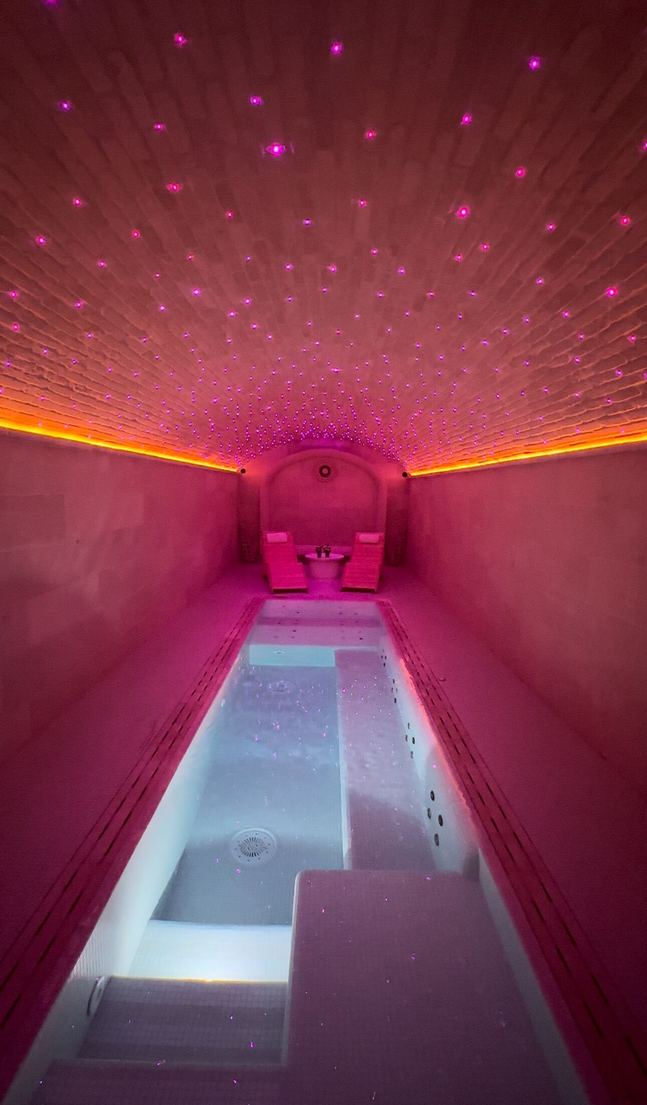 A spa room with a central water feature, pink ambient lighting, and a ceiling with small lights.