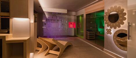 A modern spa area with a sign reading "EUPHORIA RESORT & SPA," wooden benches, a glass wall with a green-lit room, and a decorative mirror.