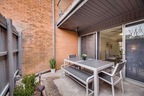 A patio with a table and chairs, a potted plant, and a sliding glass door leading to an indoor space.