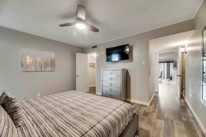A bedroom with a bed, a dresser, a ceiling fan, and a TV on the wall. - GP46A | G. Prairie Haven | 2BD | Pool | Patio (Grand Prairie)
