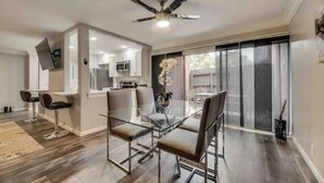 A modern kitchen with a dining area, a ceiling fan, and a sliding glass door leading to a patio. - GP46A | G. Prairie Haven | 2BD | Pool | Patio (Grand Prairie)