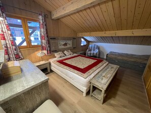 A cozy attic bedroom with a wooden ceiling, a bed with a red and white quilt, a bench, and a small table with a lamp. - Cozy 2BR Apt at Les Saisies, Close to Slopes, Sleeps 6, South Balcony, Garage Included (Les Saisies)
