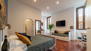 A bedroom with a bed, a bedside table with a bottle and glasses, a TV on the wall, and a window with a view. - New Charming Studio Unit in the Heart of Trastevere - Studio 1 (Roma)