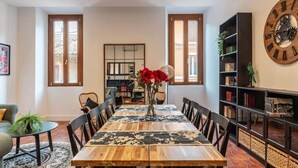A dining area with a wooden table, black chairs, and a vase with red flowers. There is a bookshelf with books and a clock on the wall. - New Charming Studio Unit in the heart Of Trastevere - Studio 2 (Roma)