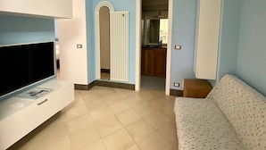 Un salon avec un téléviseur, un canapé et une cuisine visible à travers une porte ouverte.