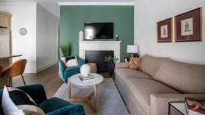 A living room with a green wall, a fireplace, a sofa, and a TV mounted above the fireplace. - The Chapel | Manor 4BR Charming Charleston (Charleston)