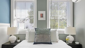A neatly made bed with white bedding, two bedside tables with lamps, and a framed picture on the wall. - The Chapel | Grand 8BR Charmer - Walkable! (Charleston)