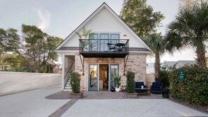 Une maison à deux étages dotée d’un balcon, d’une porte d’entrée et d’un petit espace porche aménagé avec des sièges.